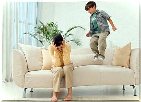 little boy jumping on sofa while mom takes care of her head