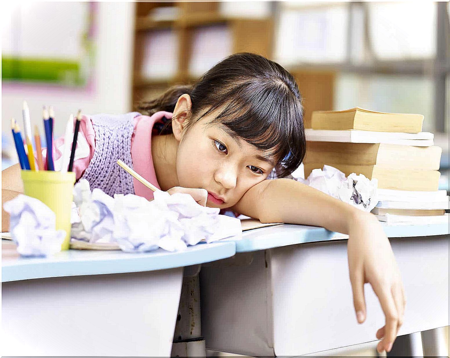 A girl with her head on her school desk surrounded by crumpled papers