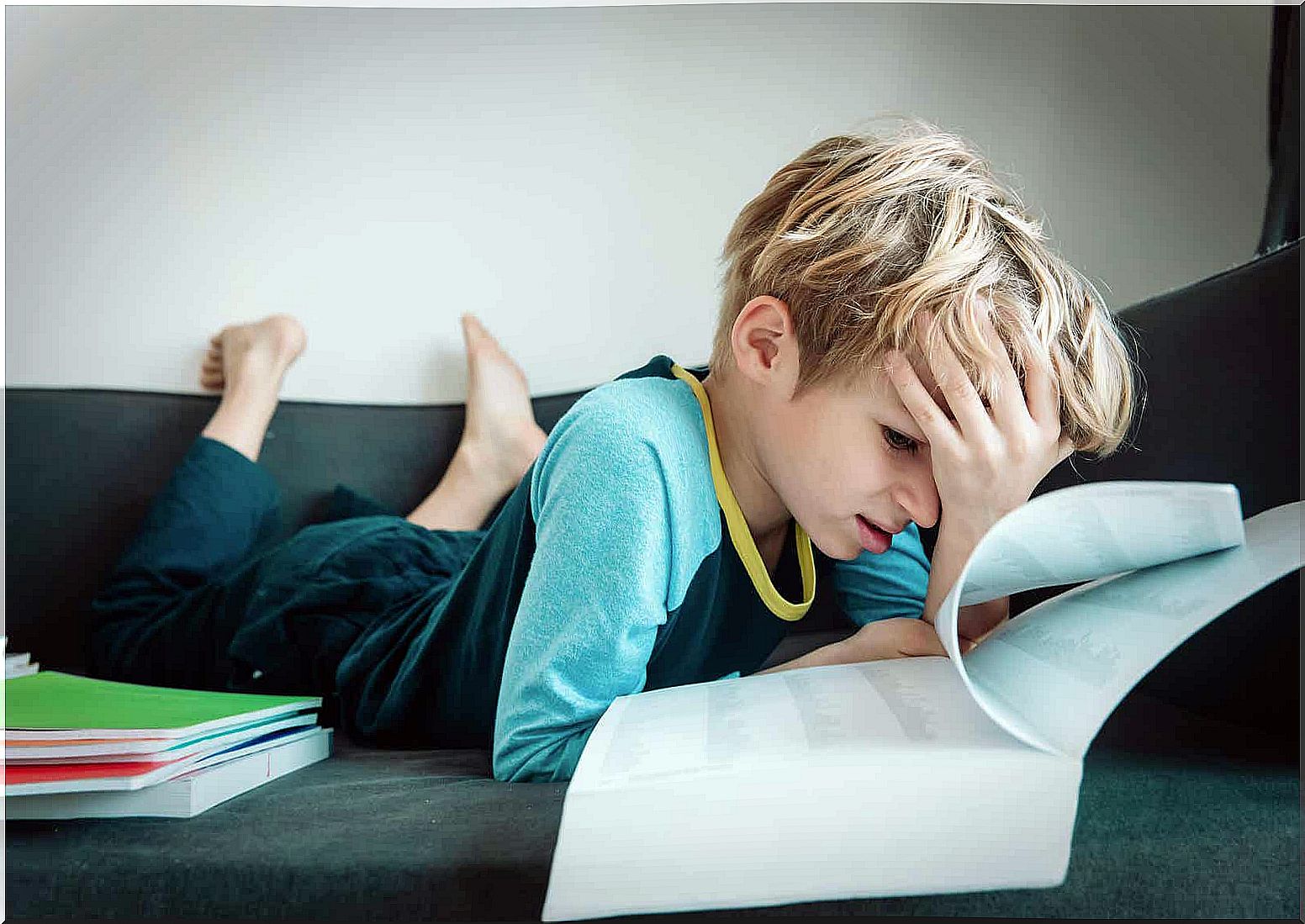 A child looks at a school book while looking with his head on his forehead frustrated