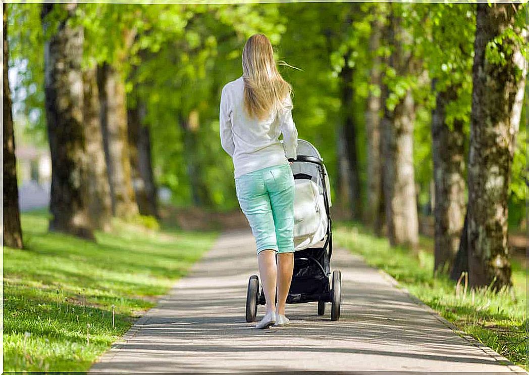 A mother walks down a path in the park with her baby in a stroller