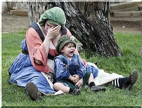 Crying baby sitting at the feet of his mother suffering from burnout