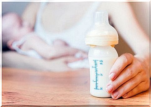 Mom holds baby bottle while breastfeeding baby