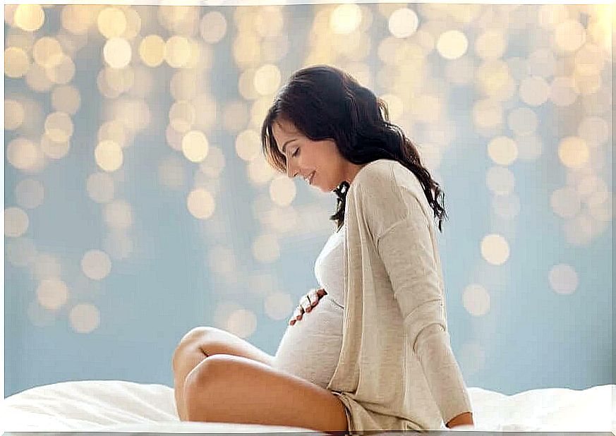 Pregnant woman sits in tailor position and holds on to her belly with a smile.